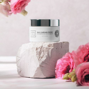 Crema facial Bulgarian Rose de Arôms Natur sobre pedestal con flores rosas