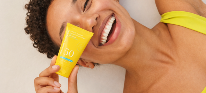 Mujer sonriendo con protector solar SPF50 en tubo amarillo
