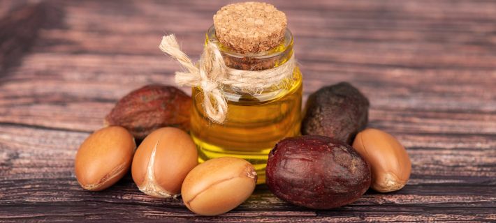 Aceite de arg&aacute;n natural en frasco con semillas alrededor sobre fondo de madera
