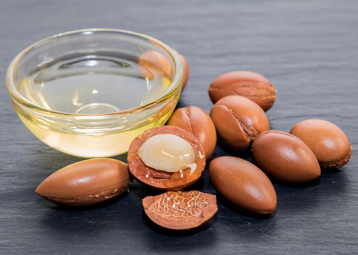 Aceite de arg&aacute;n puro en cuenco con semillas abiertas sobre mesa de madera