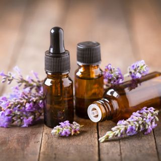 Frascos de aceite esencial de romero con flores arom&aacute;ticas sobre mesa de madera