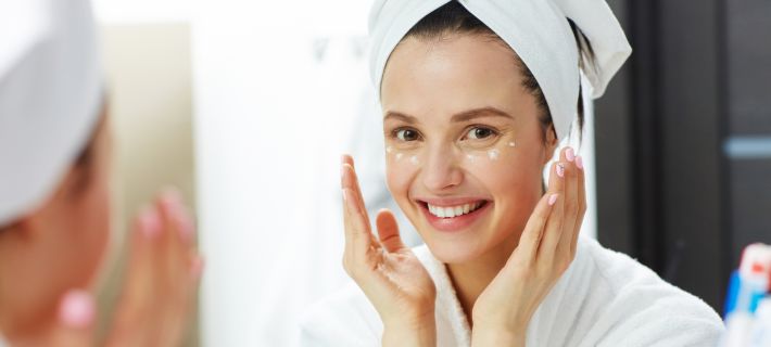 Mujer aplicando contorno de ojos frente al espejo en su rutina facial