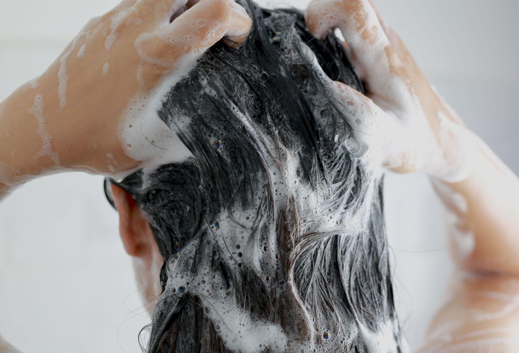 Mujer lav&aacute;ndose el cabello en la ducha con mucha espuma