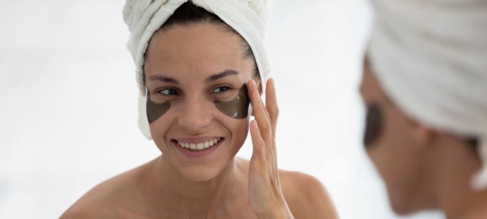 Mujer mir&aacute;ndose en el espejo con parches de hidrogel en el contorno de ojos 